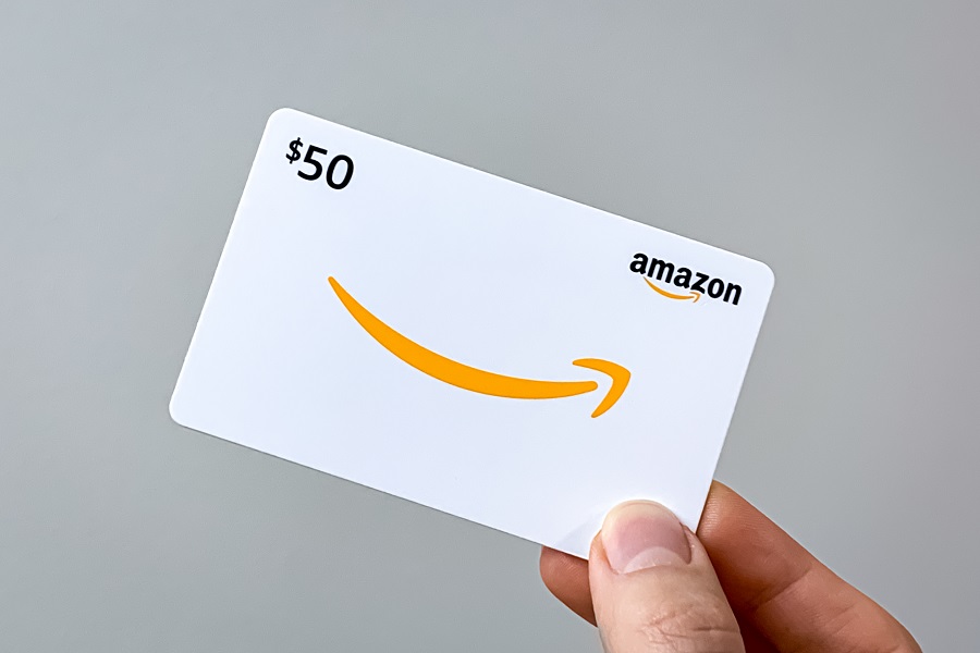 Man holding a $50 Amazon gift card against a grey background