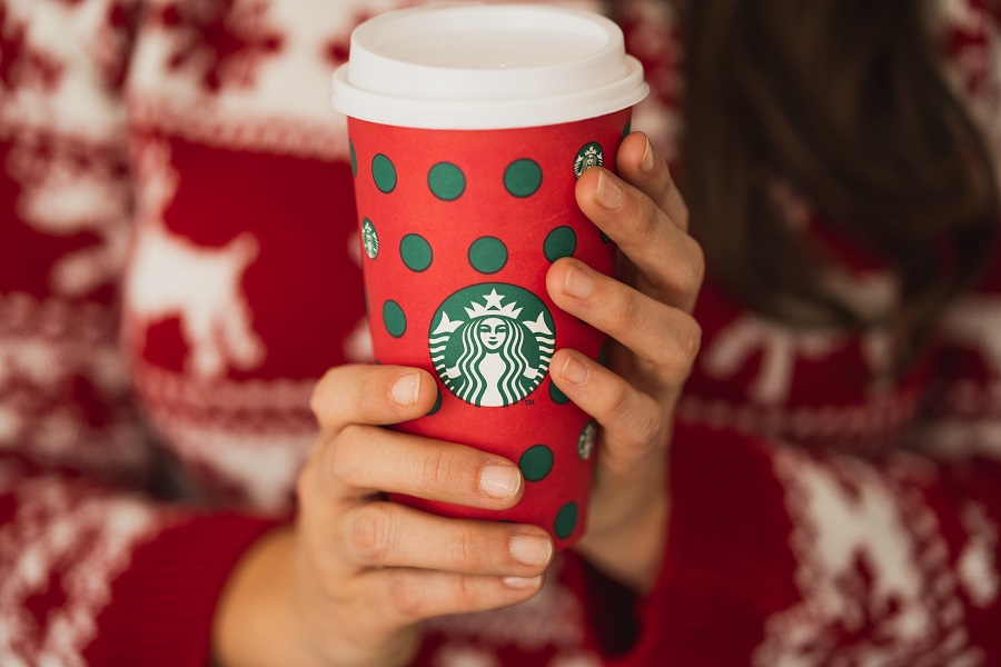 Woman with a red holiday sweater holding a holiday Starbucks cup with both hands