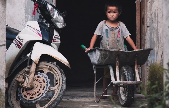 Poor boy holding a wheelbarrow in Vietnam