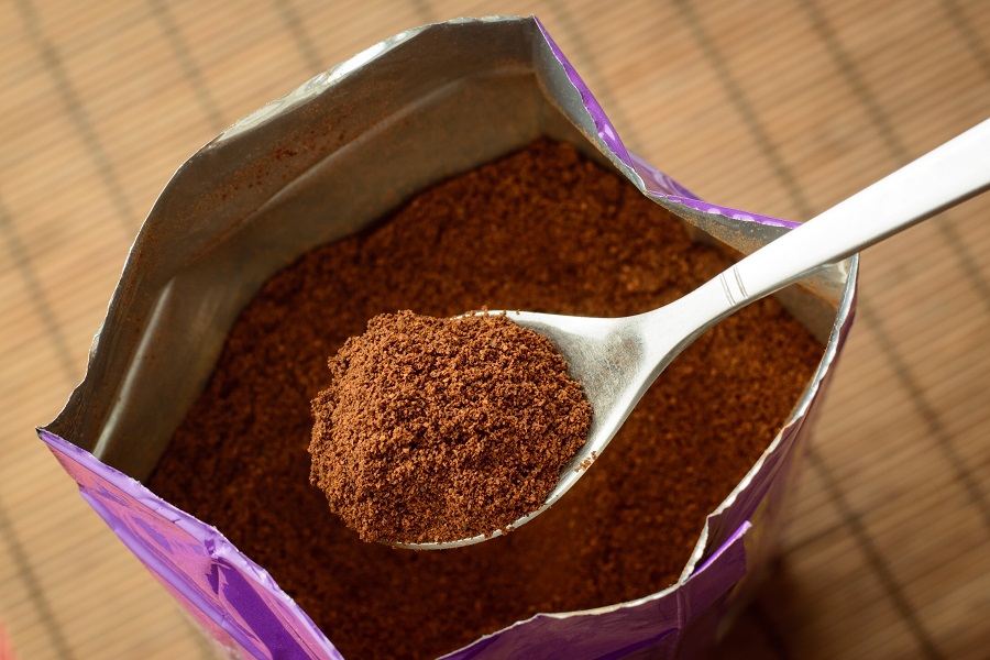 Opened ground coffee bag with some ground coffee on spoon